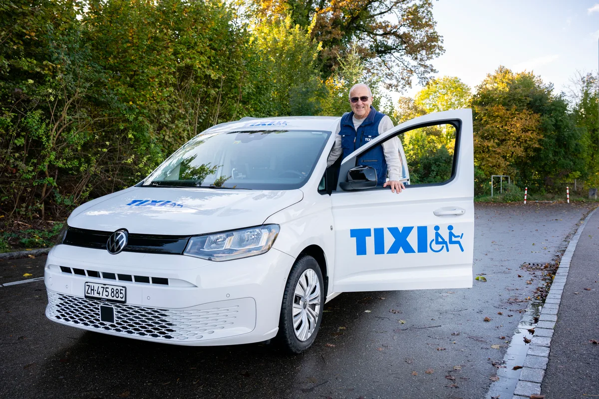 Ein Mann steht bei einem Auto, das mit Tixi beschriftet ist.